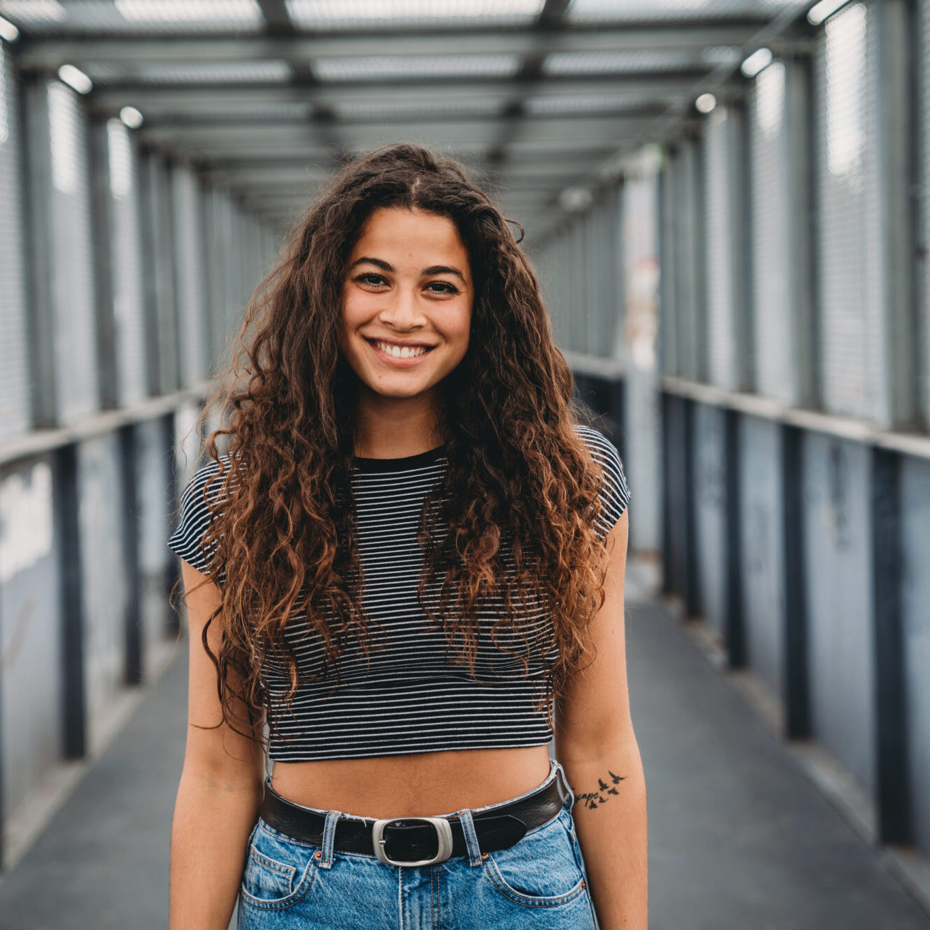 Portrait of a smiling young adult woman in the city. She's looking at camera.